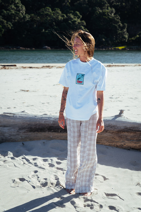 Person with the new Stamp Minus Tee from Coro Stoke is standing on a sandy beach with trees and water in the background