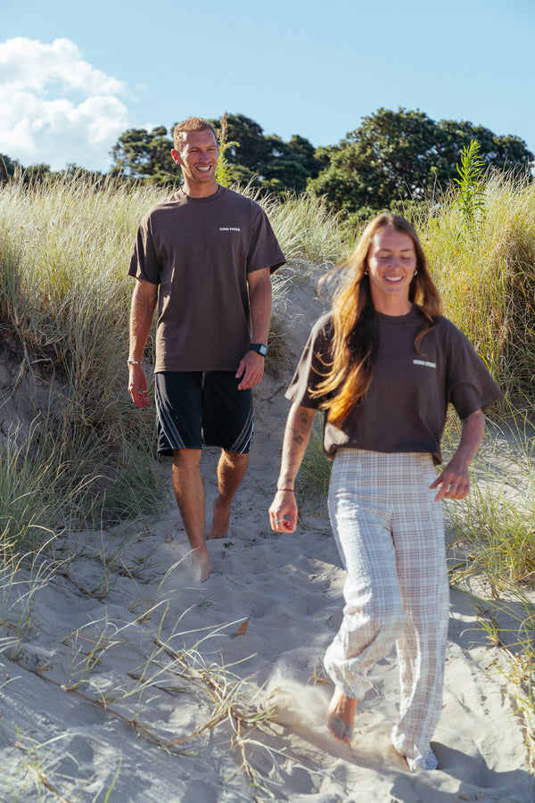 Two people with the new Wave Therapy T-Shirt from Coro Stoke, walking on a sandy path with grass and trees in the background.