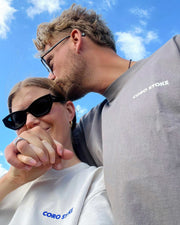 Two people wearing CORO STOKE shirts against a blue sky.