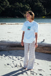 Person with the new Stamp Minus Tee from Coro Stoke is standing on a sandy beach with trees and water in the background