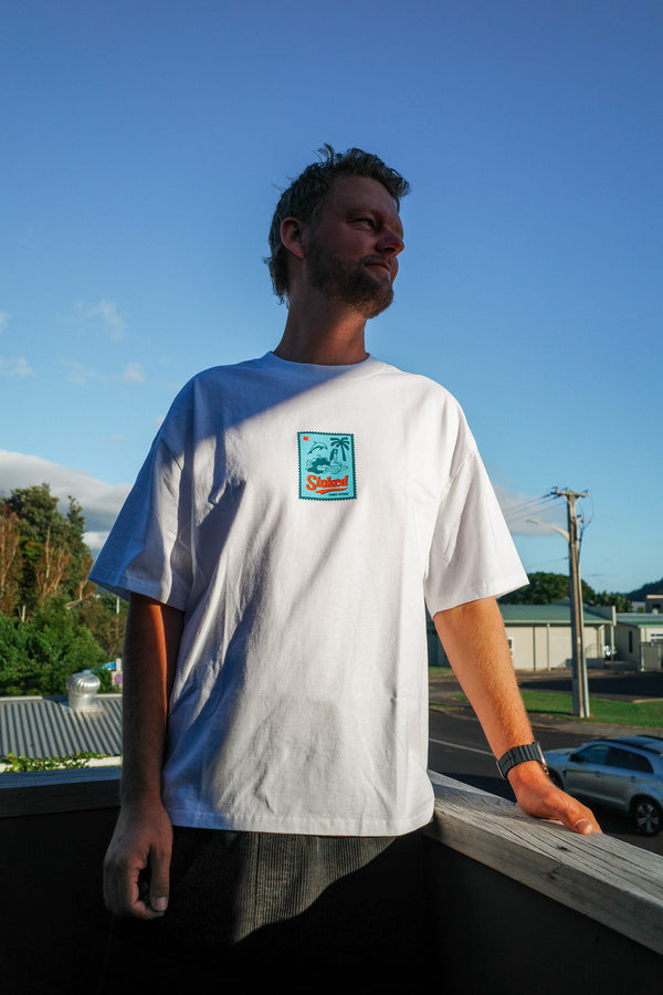 Man wearing the new Coro Stoke Stamp Minus tee with the design on the chest of the tee, standing on a rooftop with a clear blue sky.