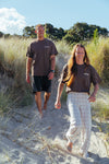 Two people with the new Wave Therapy T-Shirt from Coro Stoke, walking on a sandy path with grass and trees in the background.