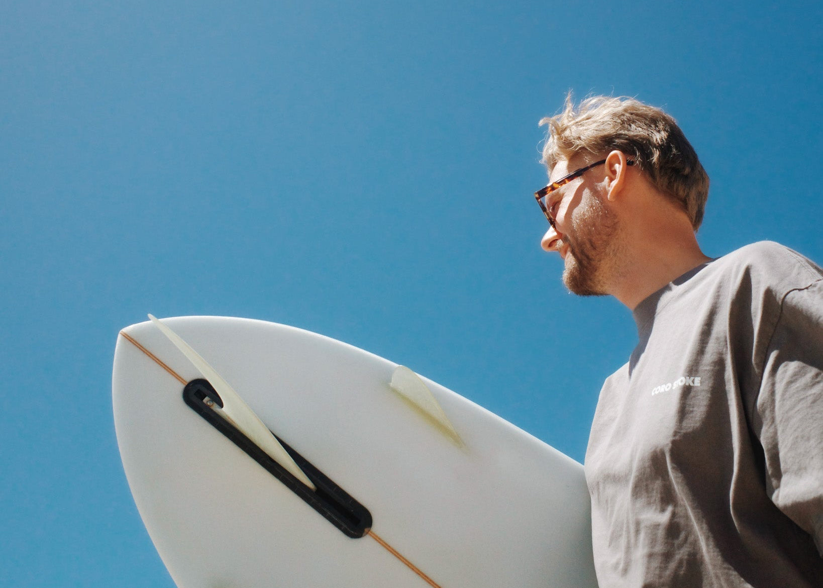 Man holding a surfboard against a clear blue sky