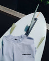 Light blue t-shirt with 'Coro Stoke' logo on a white surfboard against a dark background