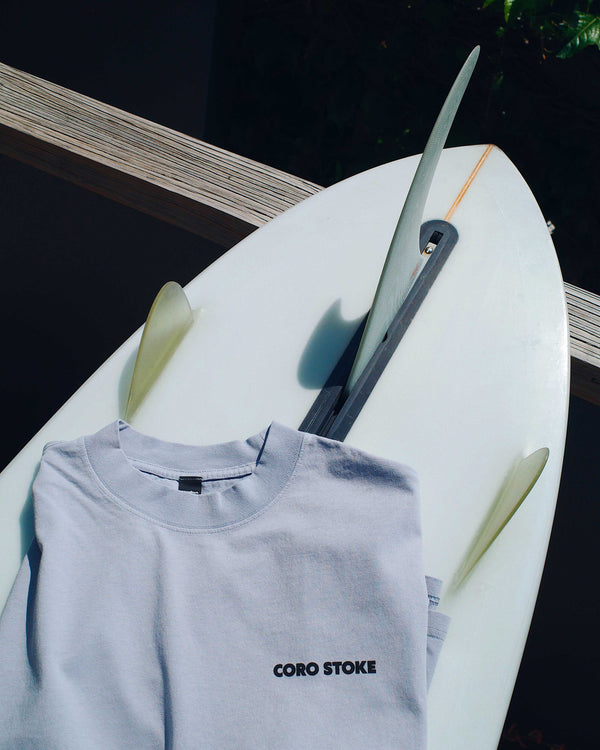 Light blue t-shirt with 'Coro Stoke' logo on a white surfboard against a dark background